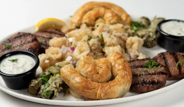 A platter of grilled meats, calamari, pastries, and dips